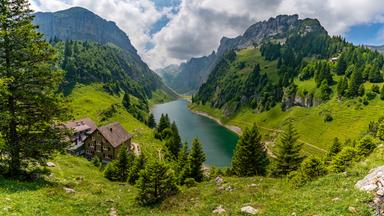 Ein atemberaubender Panoramablick auf ein üppiges Alpental mit einem ruhigen See umgeben von majestätischen Gipfeln, die Ruhe un