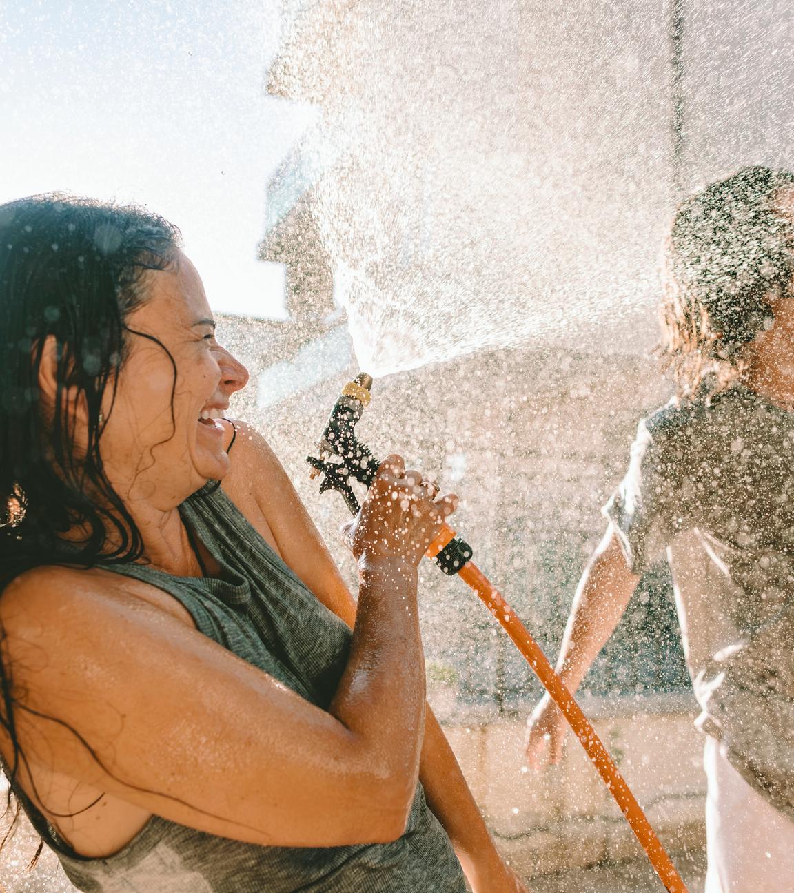 Lachende Menschen bespritzen sich draußen mit Wasser beim Sommerspaß
