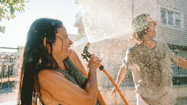 Lachende Menschen bespritzen sich draußen mit Wasser beim Sommerspaß