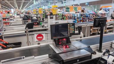 Das Bild zeigt einen leeren Supermarkt, im Vordergrund ist eine Kasse zu sehen.