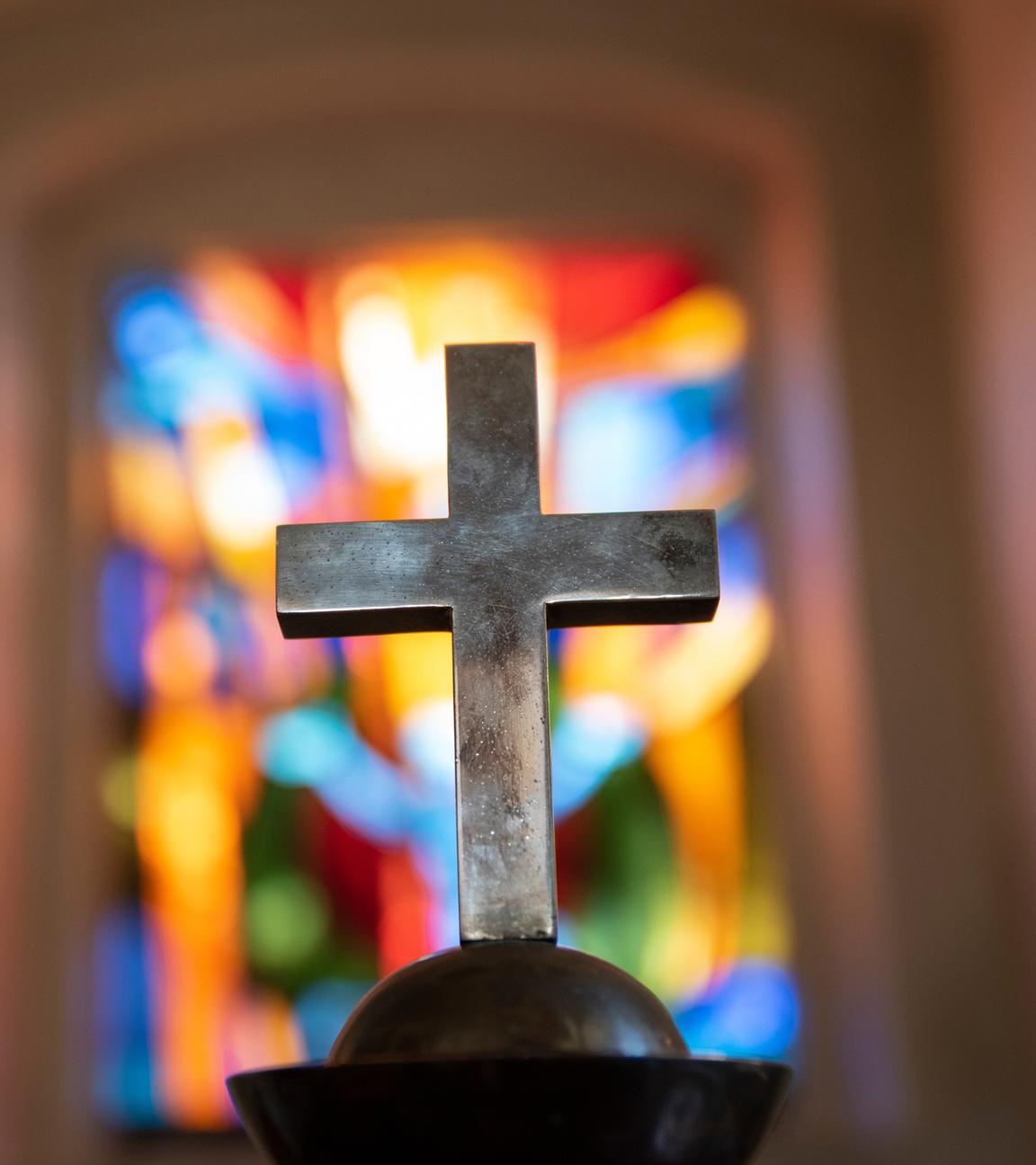 Kreuz vor buntem Kirchenfenster