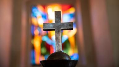 Kreuz vor buntem Kirchenfenster
