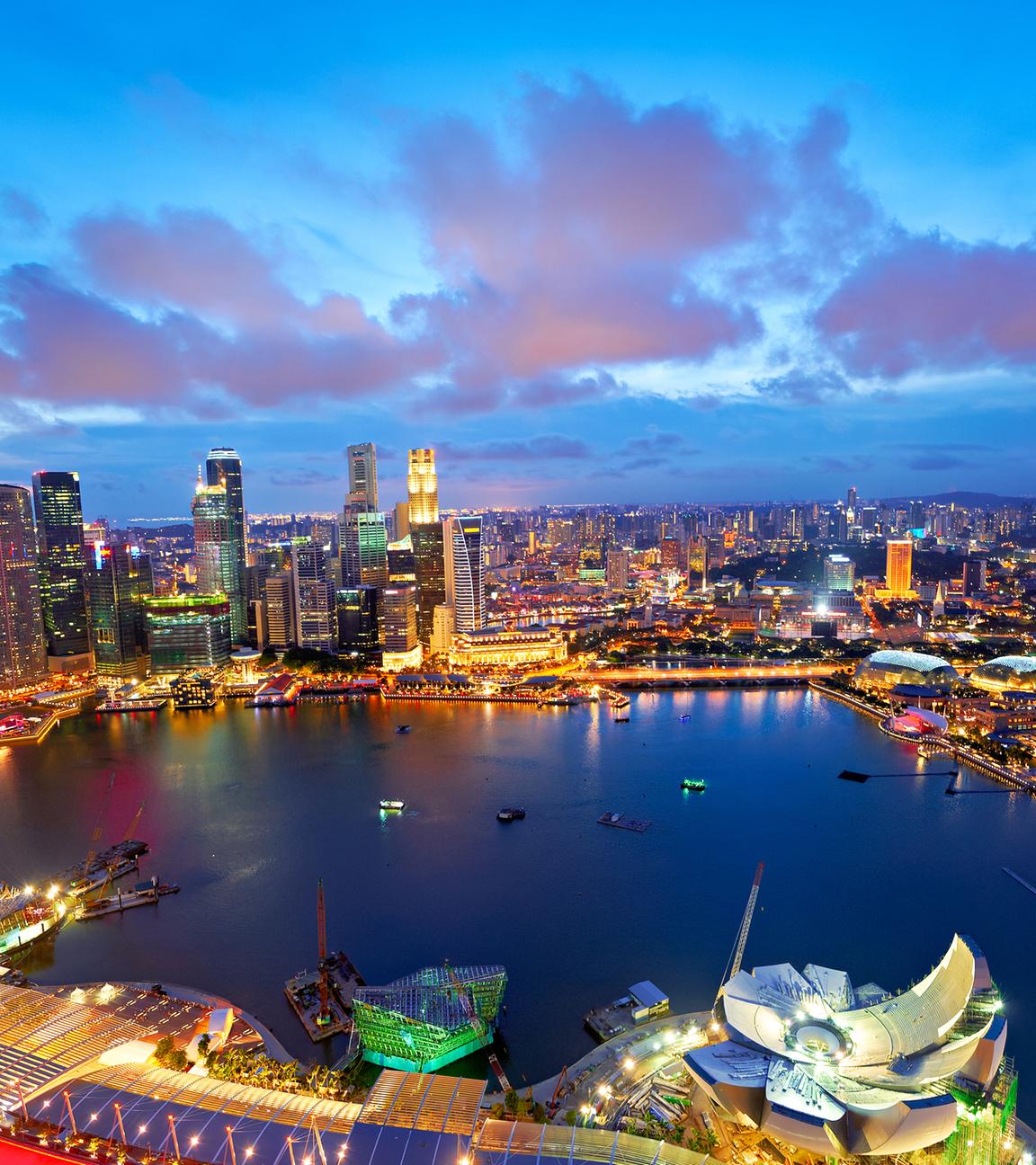 Die Lichter der Stadt leuchten bei Sonnenuntergang über der Marina Bay in Singapur.