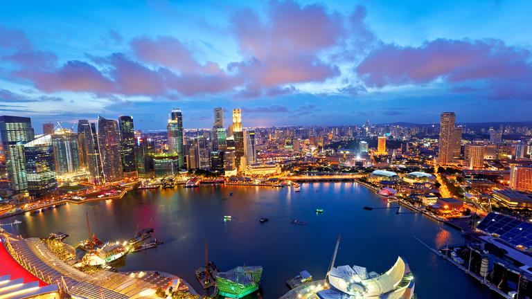 Die Lichter der Stadt leuchten bei Sonnenuntergang über der Marina Bay in Singapur.