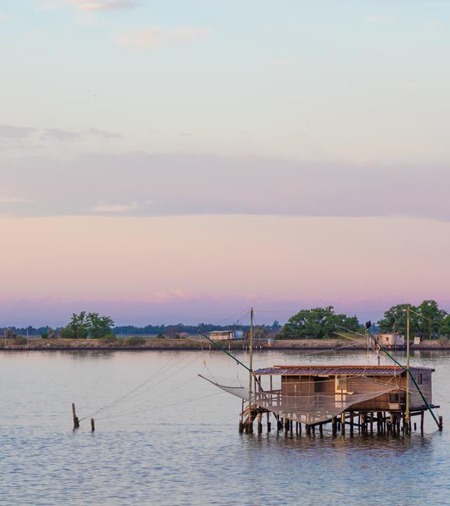 Italien, Lagune von Comacchio. Panorama mit traditionellen Haus für die Fischerei bei Sonnenuntergang, blauer Himmel