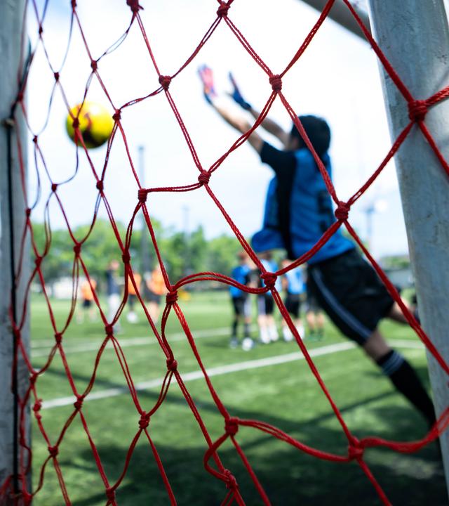 Ein Torwart, der während eines Fußballspiels einen Schuss abwehrt, aufgenommen durch das Tornetz