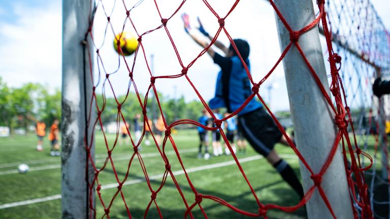 Ein Torwart, der während eines Fußballspiels einen Schuss abwehrt, aufgenommen durch das Tornetz