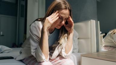Eine Frau mittleren Alters sitzt zu Hause und hält sich die Hände an die Schläfen. Kopfschmerzen, Frauengesundheit, Hormonspiege