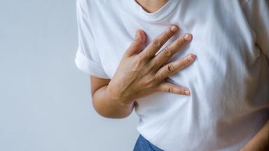Frau hält sich vornübergebeugt Hand auf die Brust- Symbolbild Asthma
