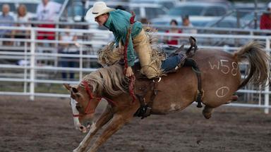 Ein Mann reitet beim Rodeo in Sutherland, Nebraska, auf einem Pferd. 