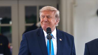 US-Präsident Trump steht vor einem Mikrofon und grinst.