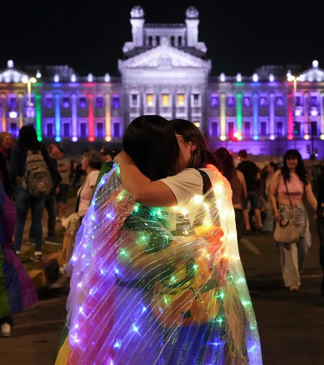 Zwei Menschen küssen sich in Regenbogenflaggen gewandt vor einer Menschenmenge beim CSD in Montevideo.