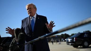 Trump steht vor Mikrofonen und wedelt ablehnend mit seinen Händen.