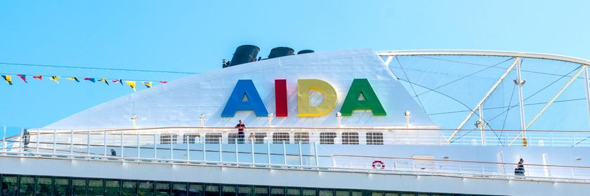 Das "AIDA"-Logo ist auf einem Schiffsdach vor blauem Himmel zu sehen.