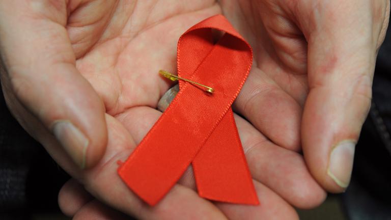 Hessen, Frankfurt/Main: Ein mit dem HI-Virus infizierter Mann hält eine rote Schleife als Symbol der Solidarität mit HIV-Positiven und Aids-Kranken.