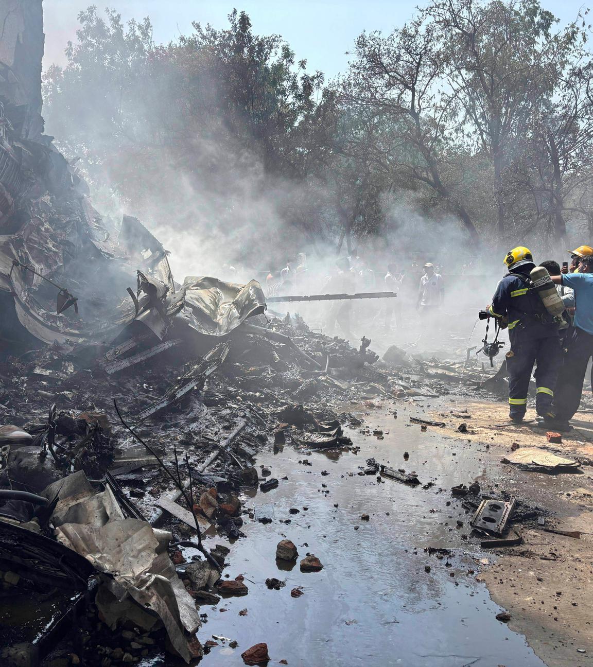 Absturzstelle des Flugzeugs an einem Haus, Verwüstung und Rauch, Feuerwehrleute stehen am rechten Bildrand.