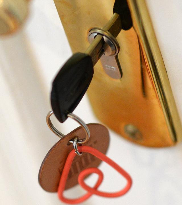 Ein Schlüsselanhänger mit dem Logo der Online-Plattform und dem Community-Marktplatz für Privatunterkünfte Airbnb hängt in Berlin an einem Schlüssel in einem Türschloss einer Ferienwohnung.