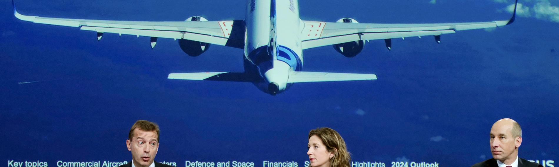 Drei Airbus-Chefs präsentieren die Jahreszahlen. Hinter ihnen ist auf einem Bild ein großes Flugzeug zu sehen. 