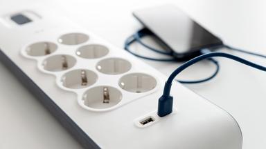 Eine Mehrfachsteckdose in die ein Smartphone mit Kabel eingesteckt ist.