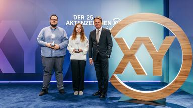 Das Bild zeigt Moderator Rudi Cerne mit zwei Preisträgern des Aktenzeichen XY-Preis.