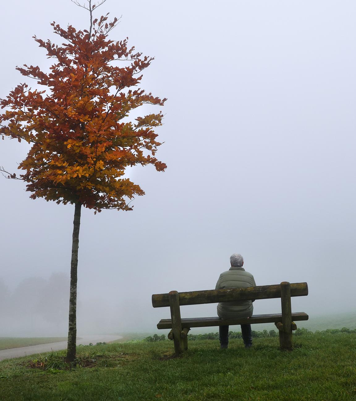 Eine Frau sitzt an einem Aussichtspunkt im Nebel auf einer Bank