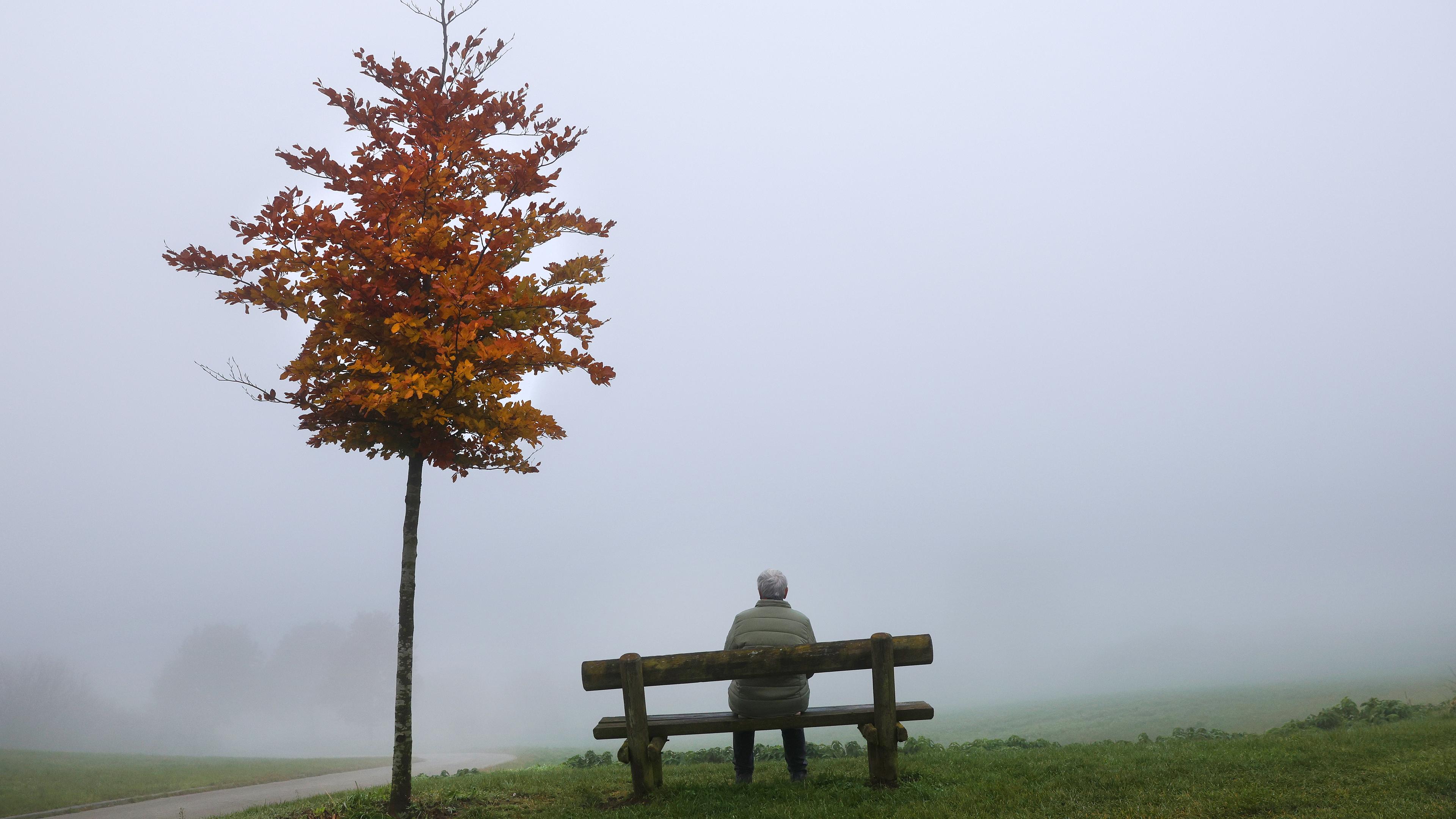 Eine Frau sitzt an einem Aussichtspunkt im Nebel auf einer Bank