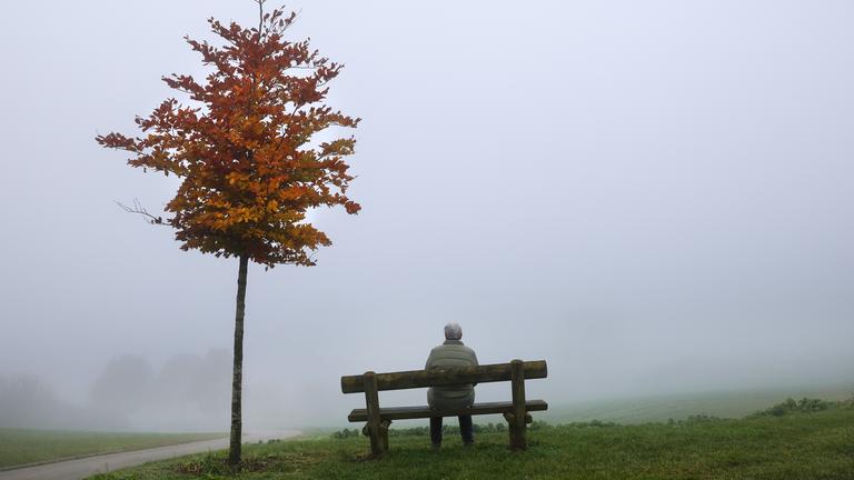 Eine Frau sitzt an einem Aussichtspunkt im Nebel auf einer Bank