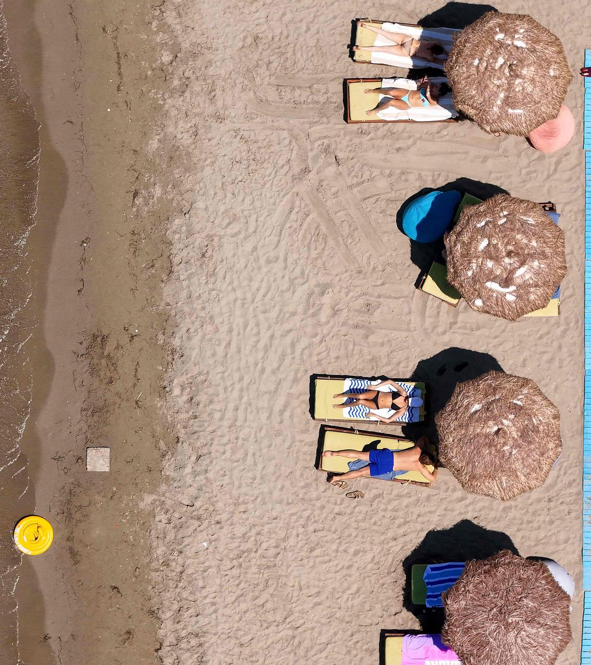 Eine Gruppe von Menschen sonnt sich am Strand in Albanien auf Sonnenliegen.
