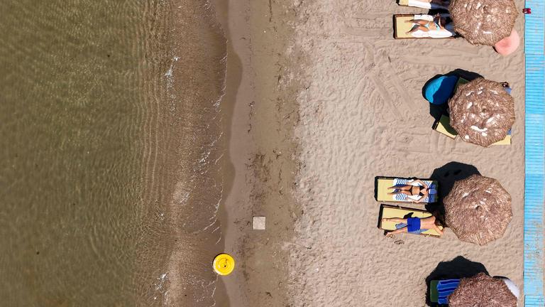 Eine Gruppe von Menschen sonnt sich am Strand in Albanien auf Sonnenliegen.