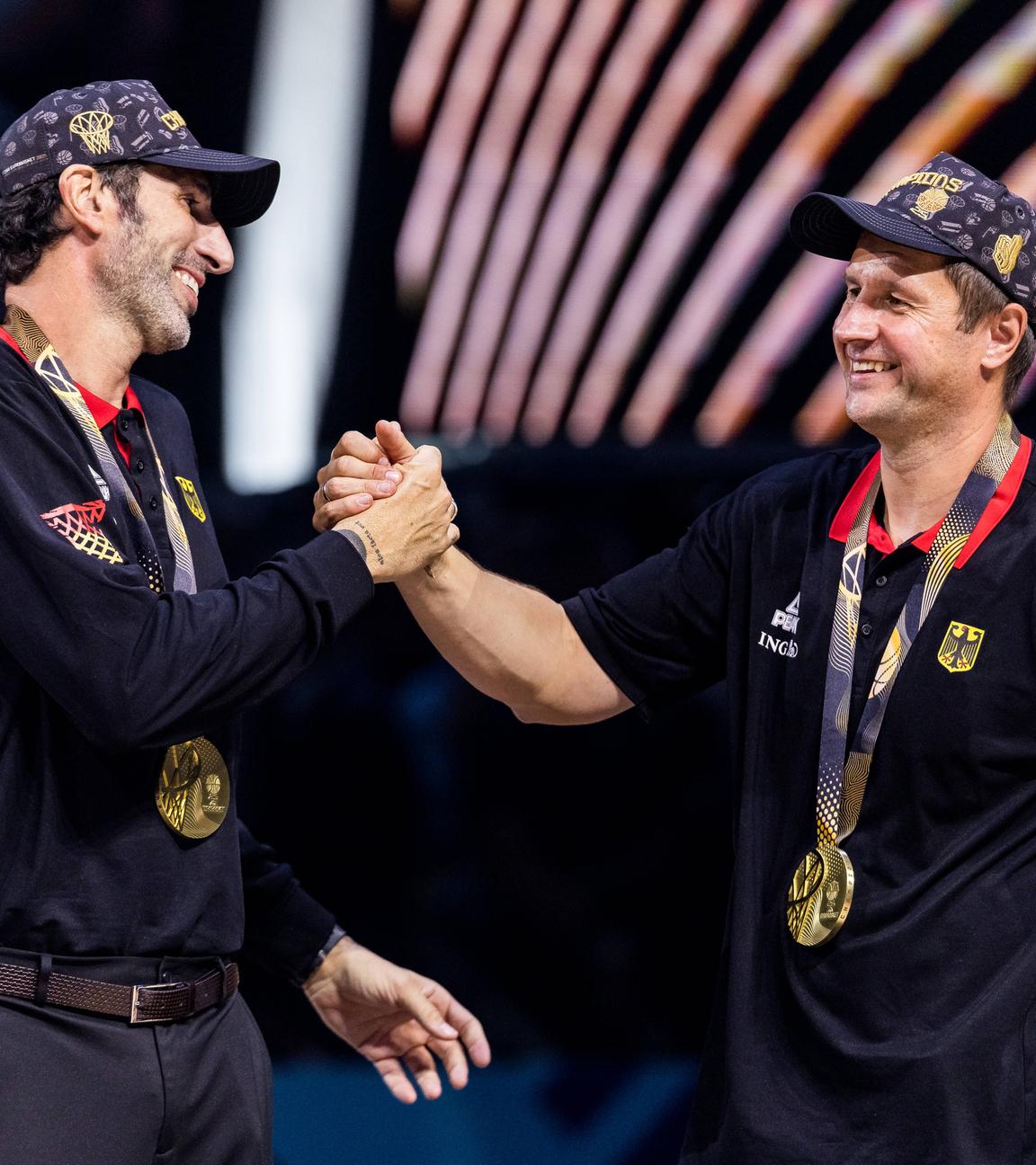 Alex Mumbru (Bundestrainer Deutschland) und Alan Ibrahimagic (Co-Trainer Deutschland) klatschen sich während des FIBA EuroBasket 2025, am 14.09.2025 in Riga, lachend ab.
