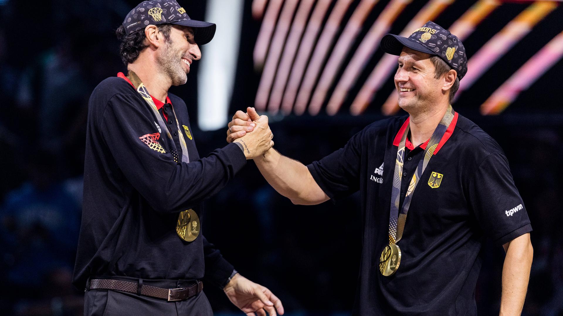 Alex Mumbru (Bundestrainer Deutschland) und Alan Ibrahimagic (Co-Trainer Deutschland) klatschen sich während des FIBA EuroBasket 2025, am 14.09.2025 in Riga, lachend ab.