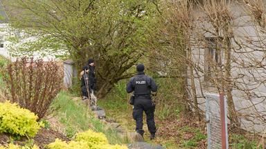 Zwei Polizisten stehen in Rahmen von Ermittlungsarbeiten an einem Haus.