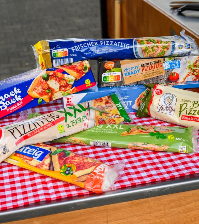 Pizzateige aus dem Kühlregal von verschiedenen Herstellern liegen auf einem Tisch.