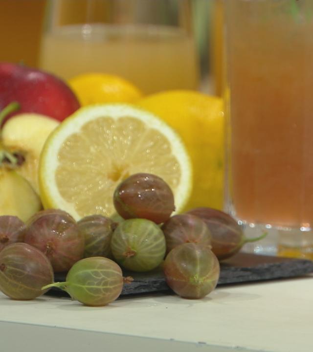 Ein alkoholfreier Bier-Cocktail im Glas und daneben Früchte, darunter Zitrone, Trauben und Apfel.