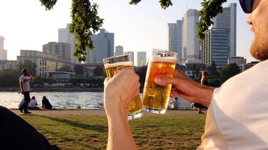 Zwei Männer stoßen in der Abendsonne mit alkoholfreiem Bier an.