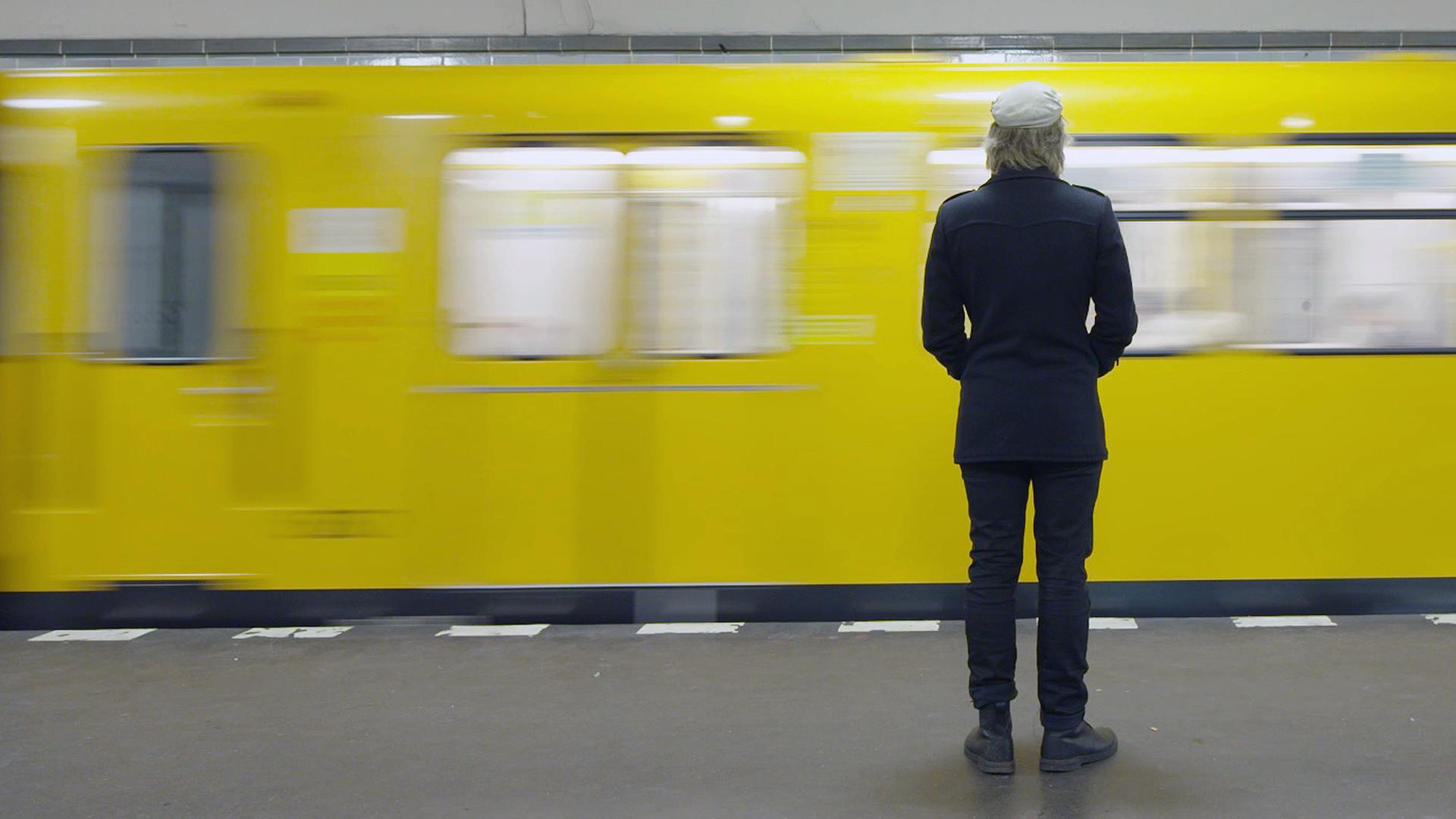 "ZDFzeit: Allein unter Millionen - Die Epidemie der Einsamkeit": Ein Mann steht alleine in einem U-Bahnhof. Vor ihm fährt gerade eine U-Bahn mit gelben Wagons vorbei.