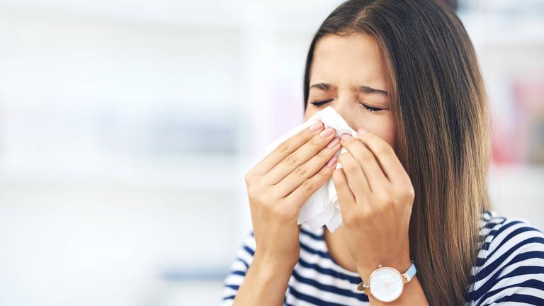Frau mit Pollenallergie hält sich Taschentuch vor die Nase, um zu niesen.