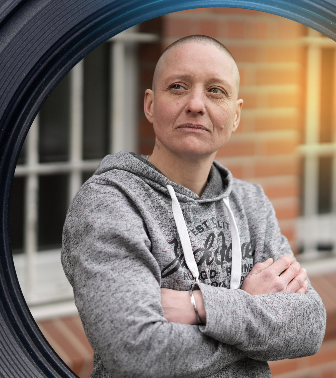 Eine Frau steht mit verschränkten Armen vor einem Gitterfenster.