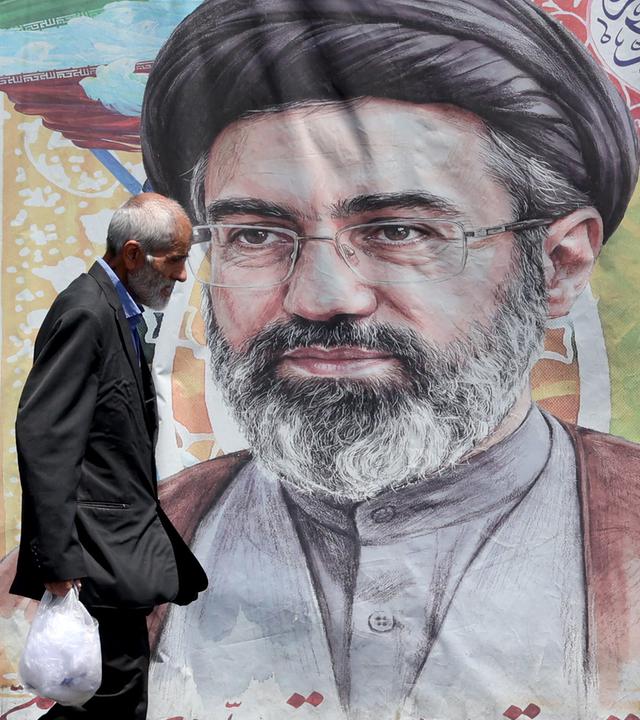 Ein iranischer Mann geht am 18. Juni 2026 in einer Straße in Teheran, Iran, an einem Plakat des iranischen Obersten Führers Ayatollah Mojtaba Khamenei vorbei.