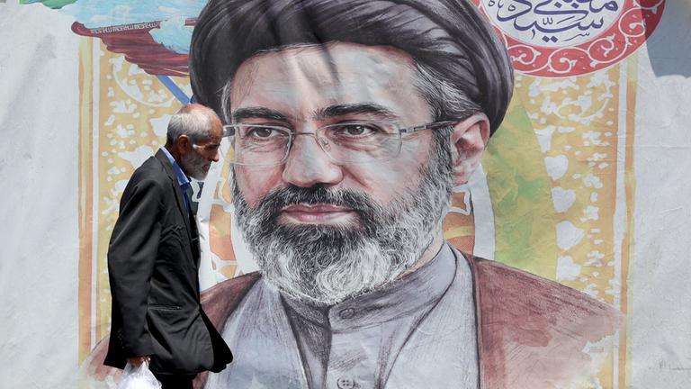 Ein iranischer Mann geht am 18. Juni 2026 in einer Straße in Teheran, Iran, an einem Plakat des iranischen Obersten Führers Ayatollah Mojtaba Khamenei vorbei.