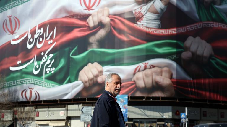 Ein Iraner läuft neben einer Werbetafel am 16.01.2026 auf der "Iran ist unsere Heimat" am Enqelab-Platz  in Teheran, Iran, steht.