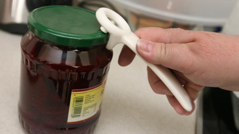 Eine Frau versucht mit einem am Deckel angesetzten Spezial-Öffner ein Schraubglas zu öffnen.