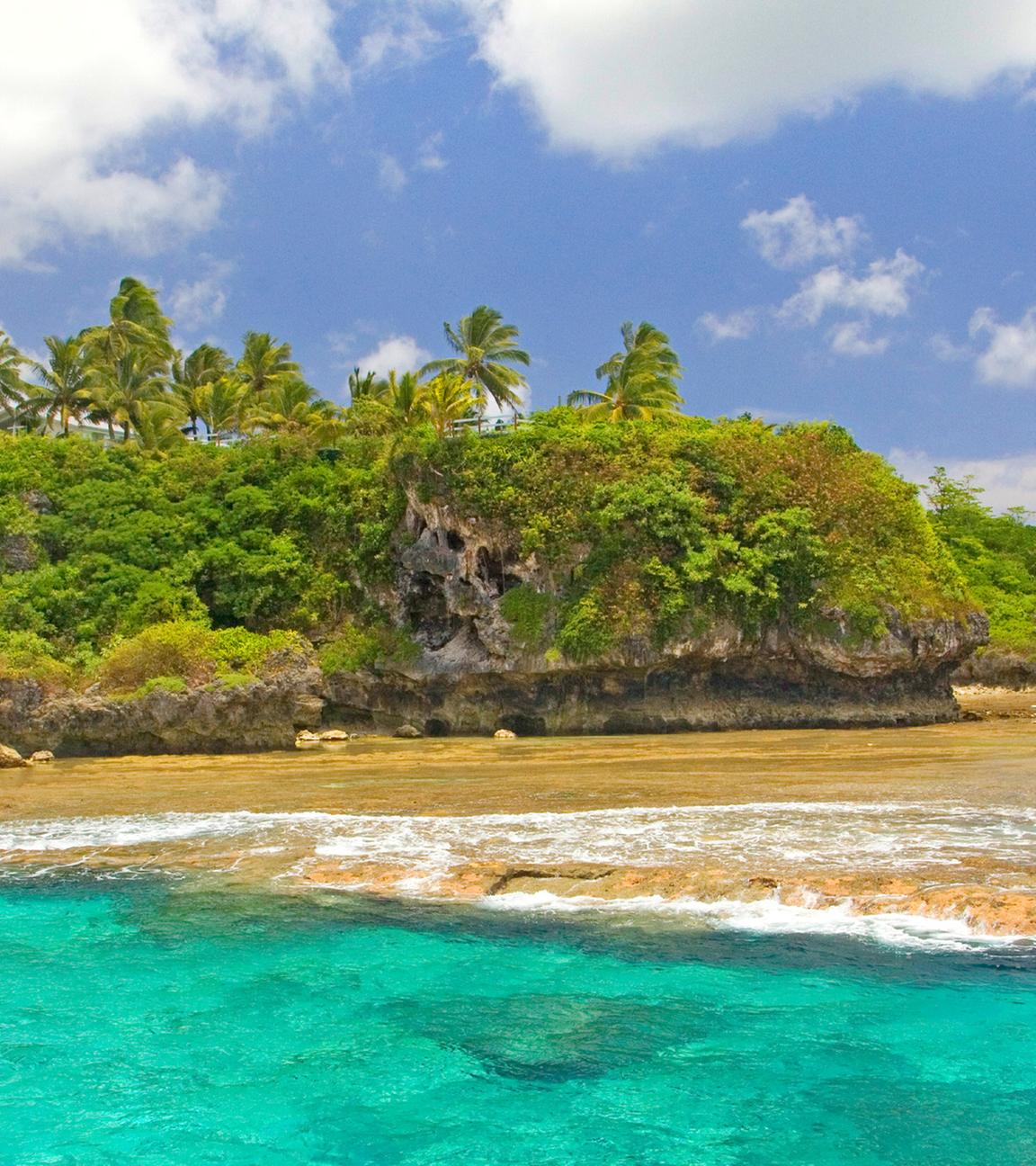 Küste von Alofi mit Palmen und Stradt im pazifischen Inselstaat Niue. 