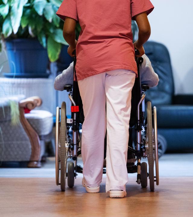 Eine Bewohnerin eines Pflegeheims wird von einer Pflegerin einen Gang entlang geschoben