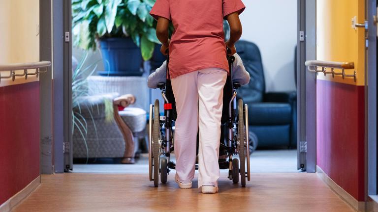 Eine Bewohnerin eines Pflegeheims wird von einer Pflegerin einen Gang entlang geschoben