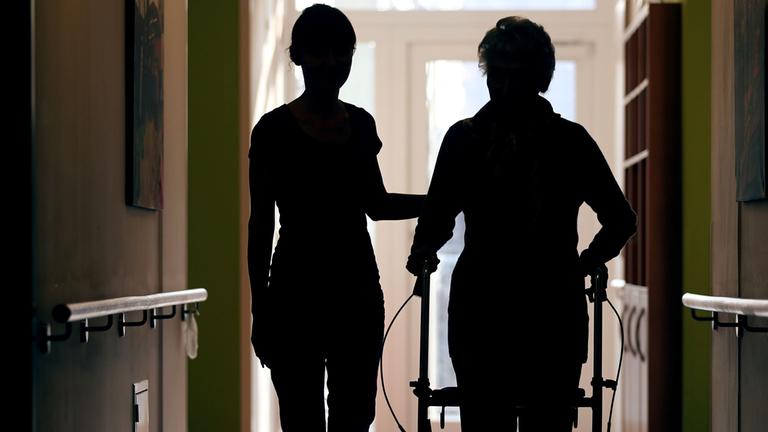 Archiv: Eine Pflegekraft begleitet am 22.02.2013 in Köln die Bewohnerin eines Altenheims beim Gang über den Flur 