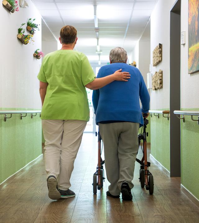 Niedersachsen, Nienburg: Eine Pflegefachkraft geht mit einer Bewohnerin durch ein Seniorenheim