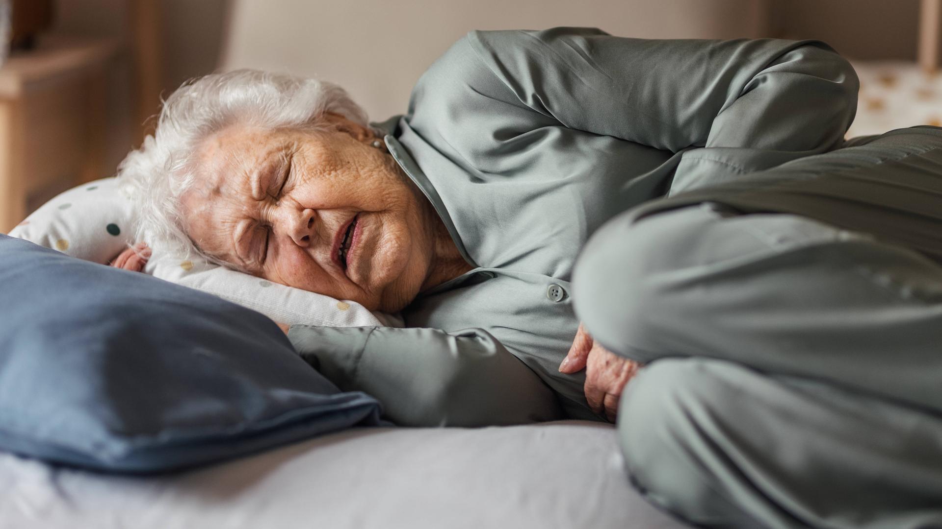 Eine ältere Frau liegt seitlich im Bett und versucht zu schlafen. Ihr Gesichtsaudruck deutet auf Schmerzen hin. 