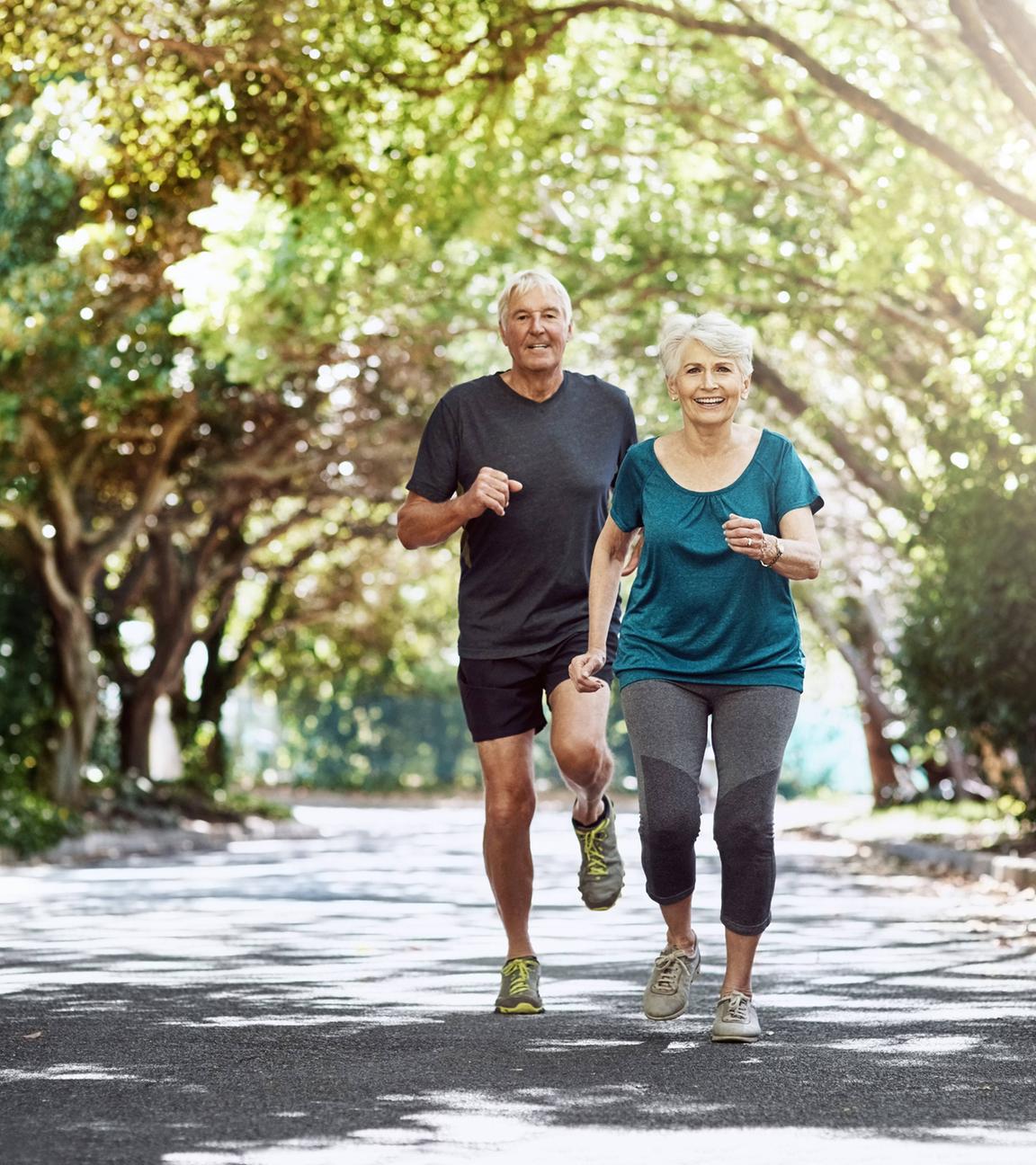 Älteres Paar joggt durch einen Park.