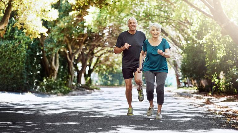 Älteres Paar joggt durch einen Park.